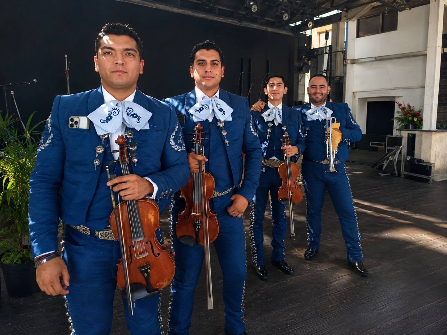 Cuatro integrantes del mariachi con violines y trompeta en un escenario